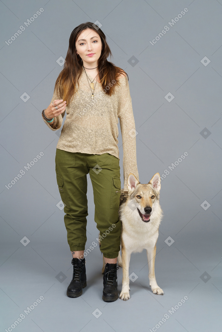 A figura intera di un maestro femmina in piedi accanto al suo cane e guardando la fotocamera