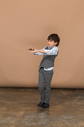 Vista frontal de um menino de terno em pé com os braços estendidos