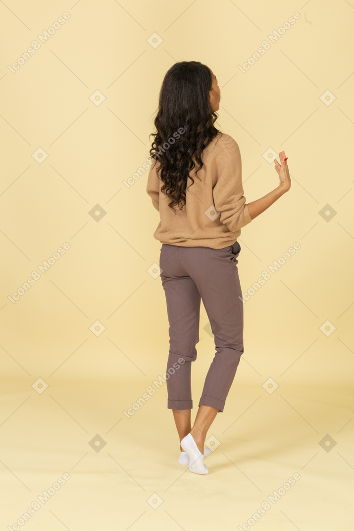 Vista posterior de tres cuartos de una mujer joven de piel oscura que respira pesadamente agitando sus manos
