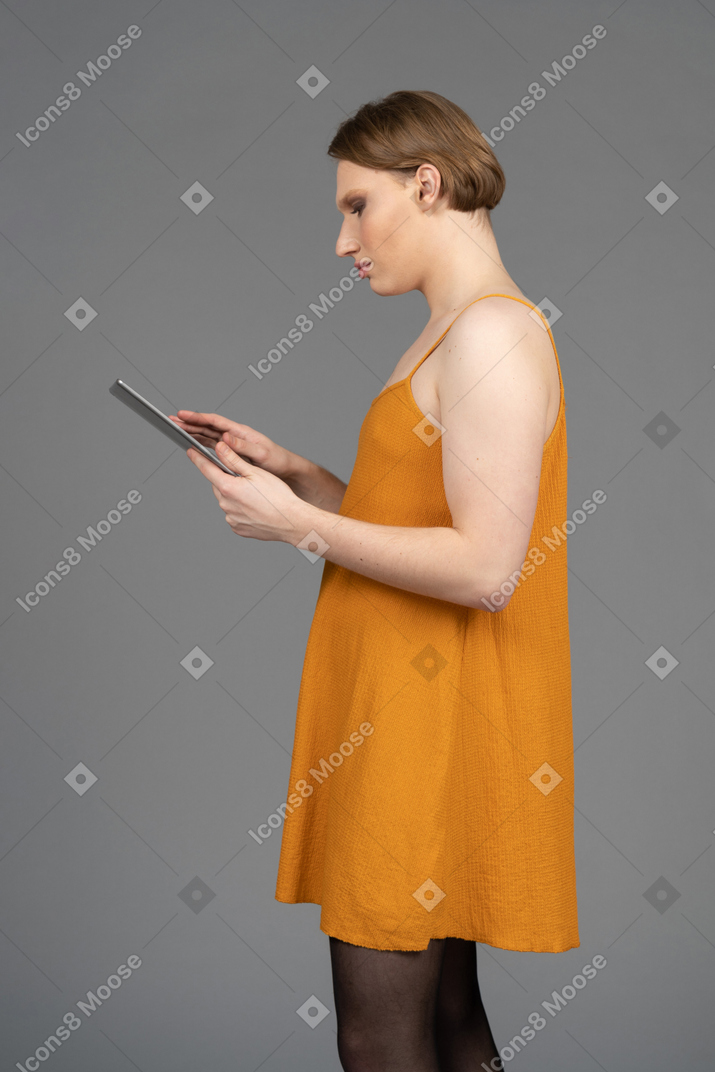 Young transgender person in orange dress using digital tablet
