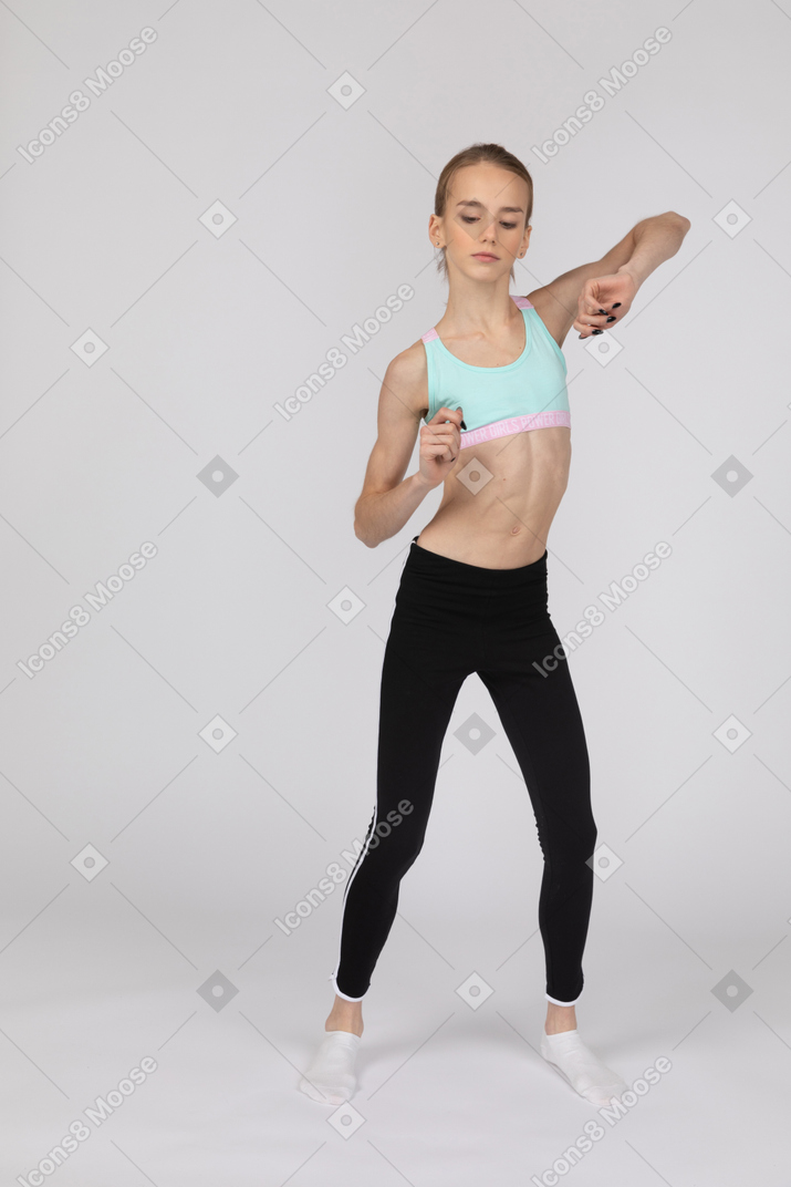 Девушка в спортивной одежде в полный рост поднимает руки и танцует