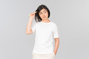 Pensive young indian woman touching hair with a toothbrush
