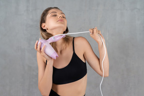 Young woman tightening hairdryer cord around her neck