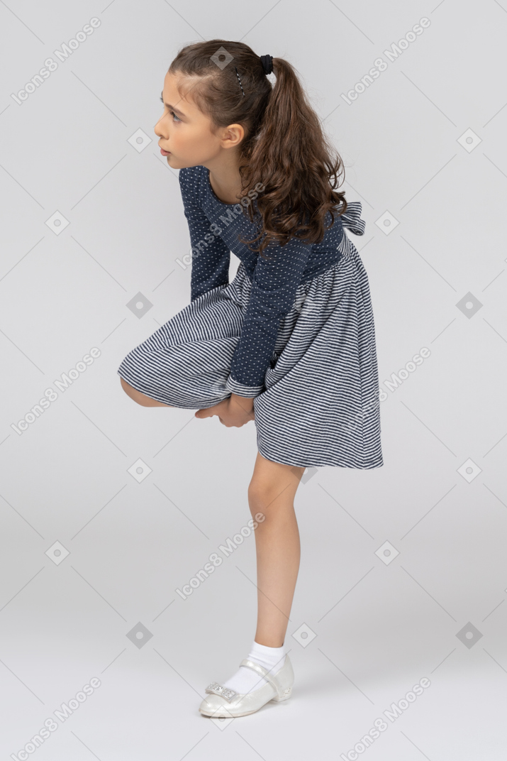 Vista posteriore di tre quarti di una ragazza che rimbocca la gamba mentre è in piedi