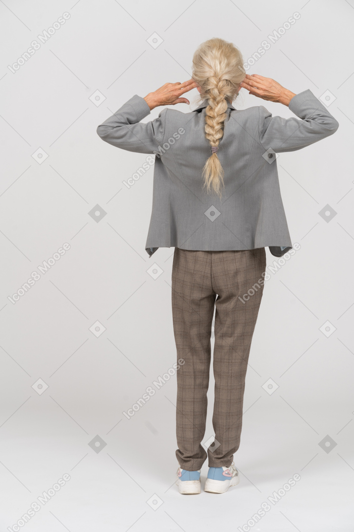 頭の後ろに手を置いて立っているスーツを着たおばあさんの背面図