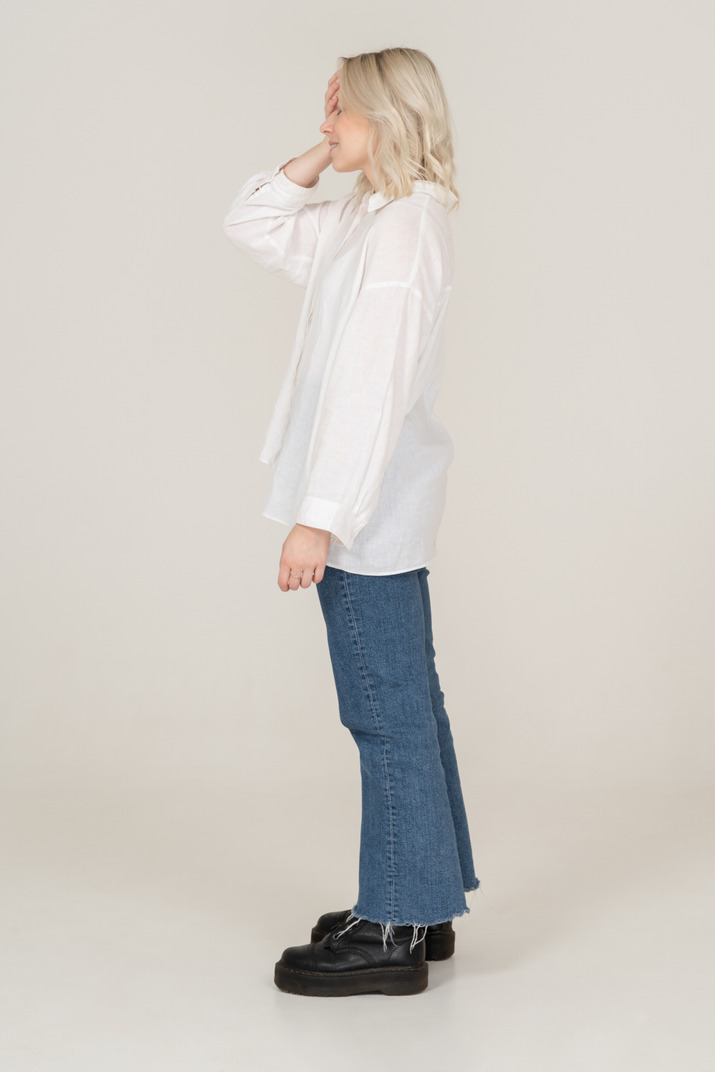 Side view of a blonde female in casual clothes standing still and hiding face