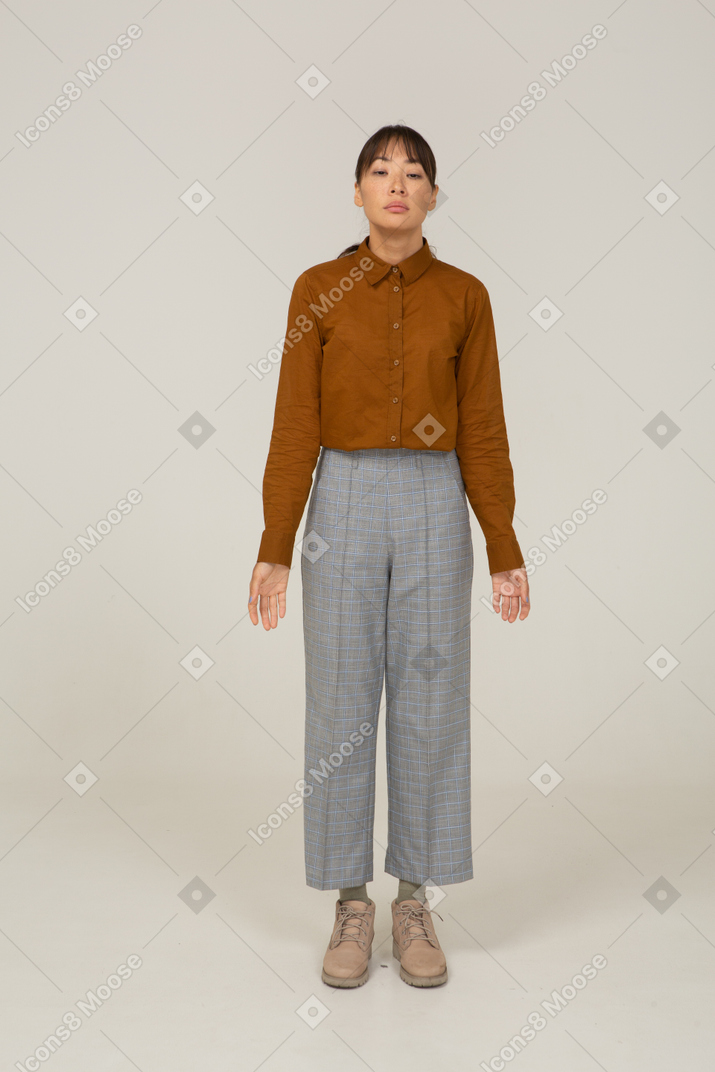Vista frontale di una giovane donna asiatica in calzoni e camicetta in piedi ancora