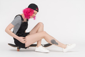 Mädchen sitzt auf einem skateboard und schaut auf ihre beine
