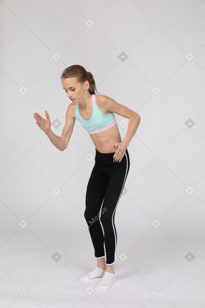 Three-quarter view of a teen girl in sportswear leaning forward while standing like a robot