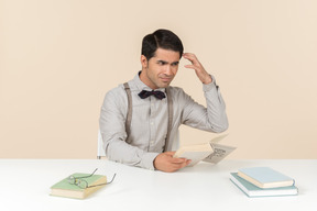 Angry adult professor sitting at the table and reading a book