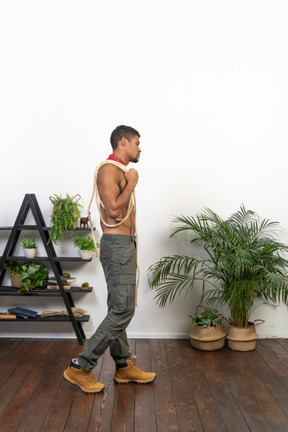 Side view of muscular young man with a coil of rope on his shoulder walking