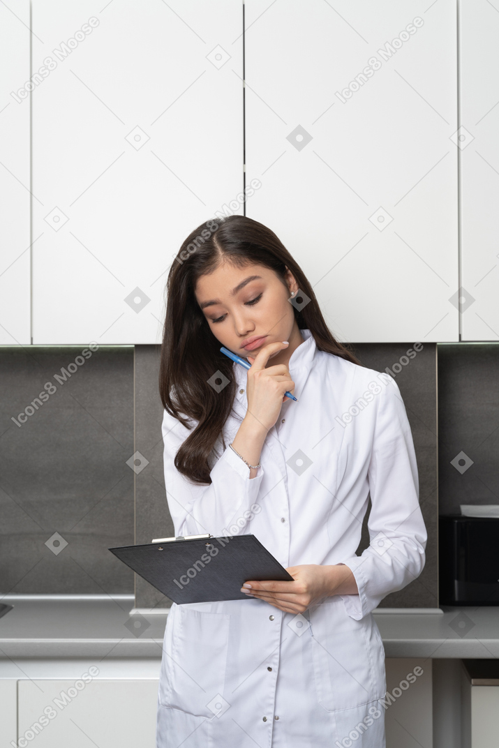 Front view of a puzzled female doctor touching chin and looking down at the tablet