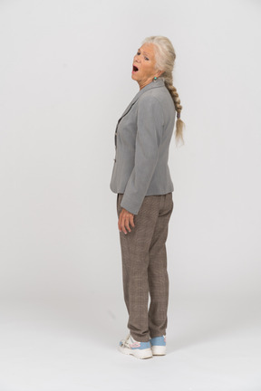 Вид сзади эмоциональной старушки в костюме, стоящей с открытым ртом