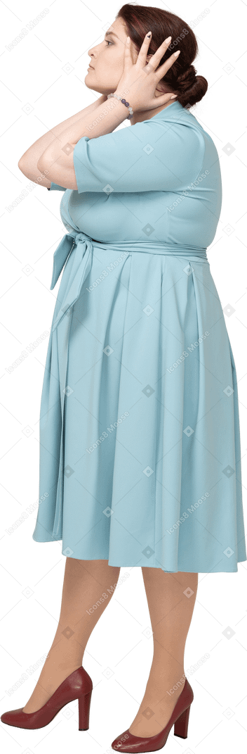 Vista lateral de una mujer en vestido azul cubriendo las orejas con las manos