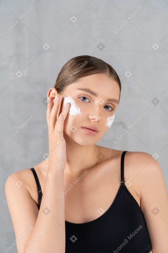 Portrait of a young woman applying face cream on her cheeks