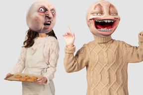 A woman with a tray of cookies and a man wearing rage comic masks