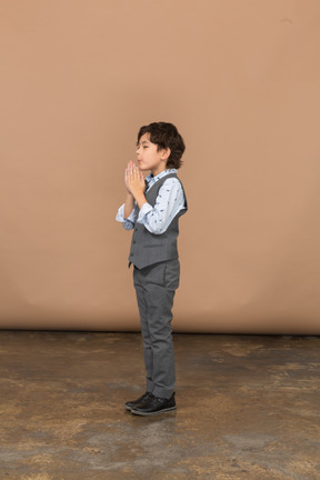 Vista lateral de un niño en traje haciendo gesto de oración