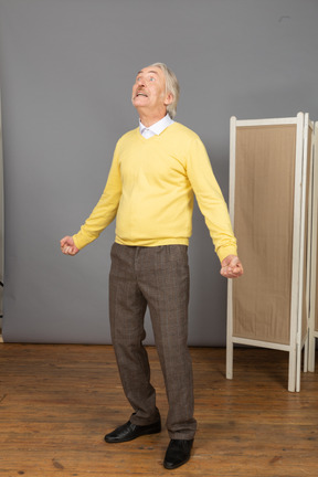 Vista de tres cuartos de un anciano gritando extendiendo las manos mientras mira hacia arriba