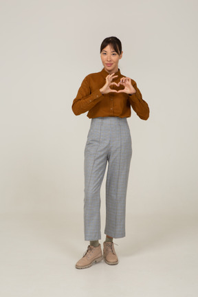 Front view of a young asian female in breeches and blouse showing heart gesture