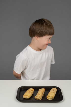 Seitenansicht eines kleinen jungen, der vor einem essenstablett grinst