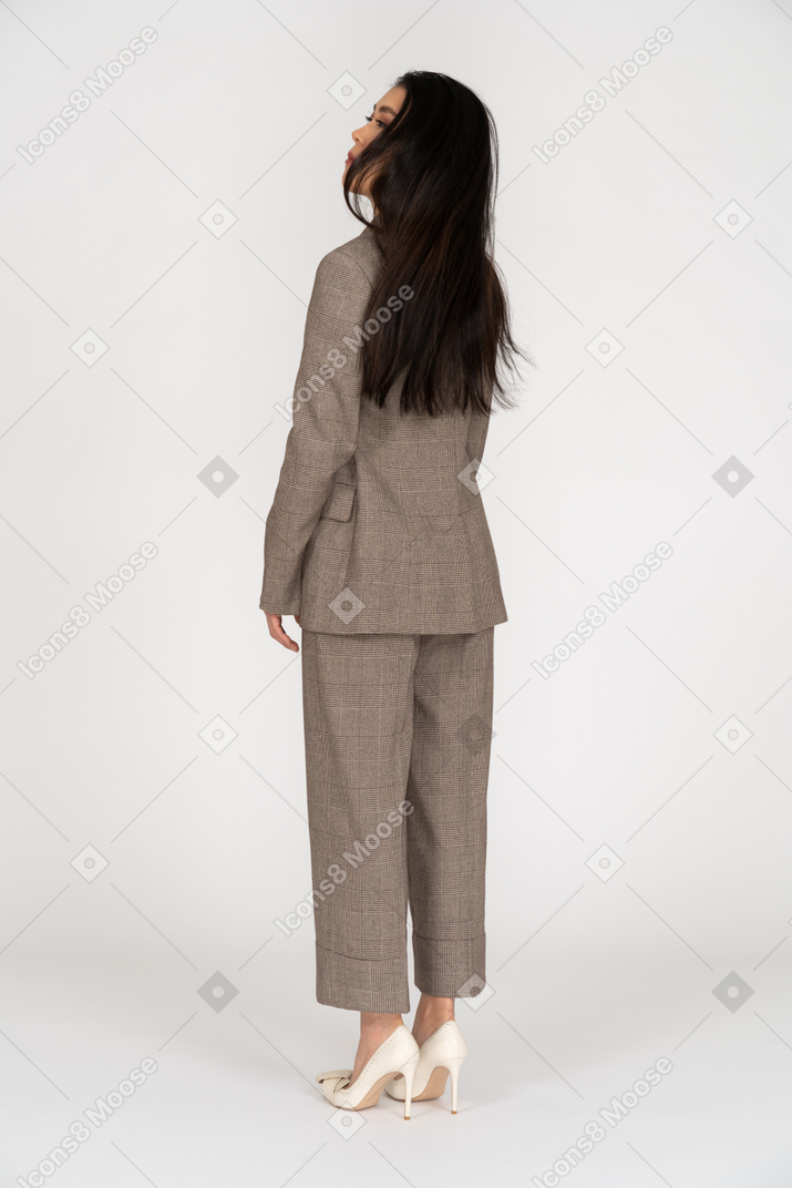 Three-quarter back view of a young lady in brown business suit turning away