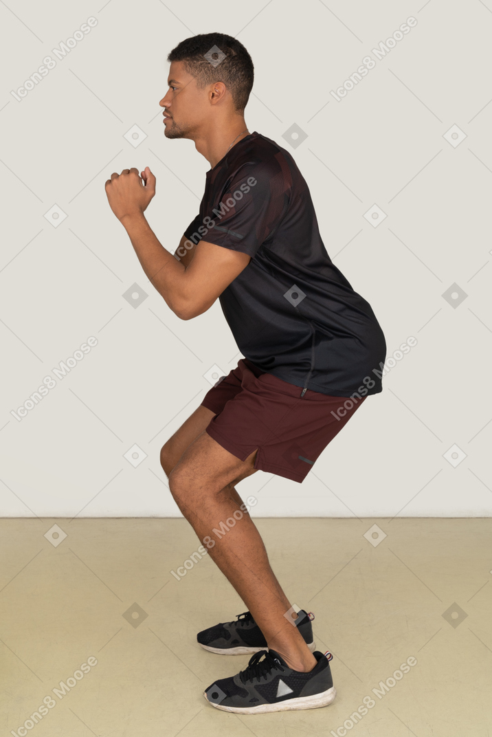 Молодой человек в спортивной одежде сидит на корточках