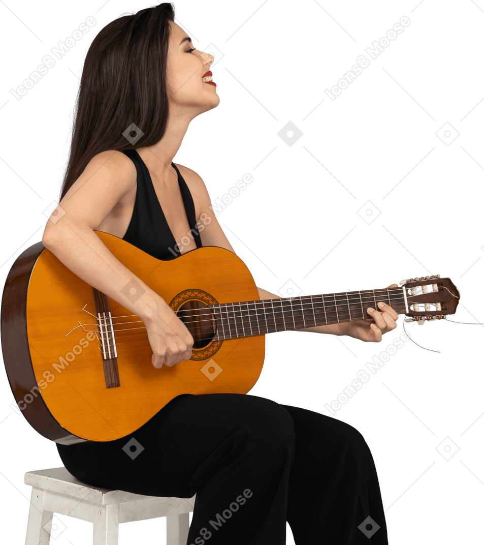 Side view of a sitting smiling young lady in black suit playing guitar