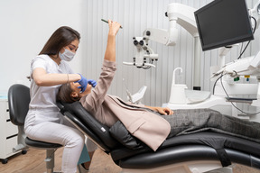 Женщина-стоматолог в полный рост осматривает своего пациента, делая селфи