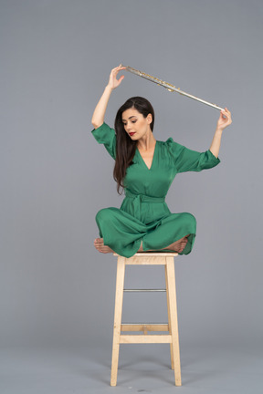 Pleine longueur d'une jeune femme tenant sa clarinette au-dessus de la tête alors qu'il était assis sur une chaise en bois