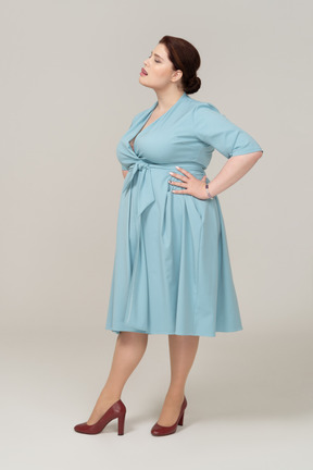 Vista laterale di una donna in abito blu in posa con le mani sui fianchi