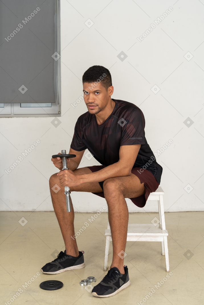 Young man in sports clothes sitting on white stool