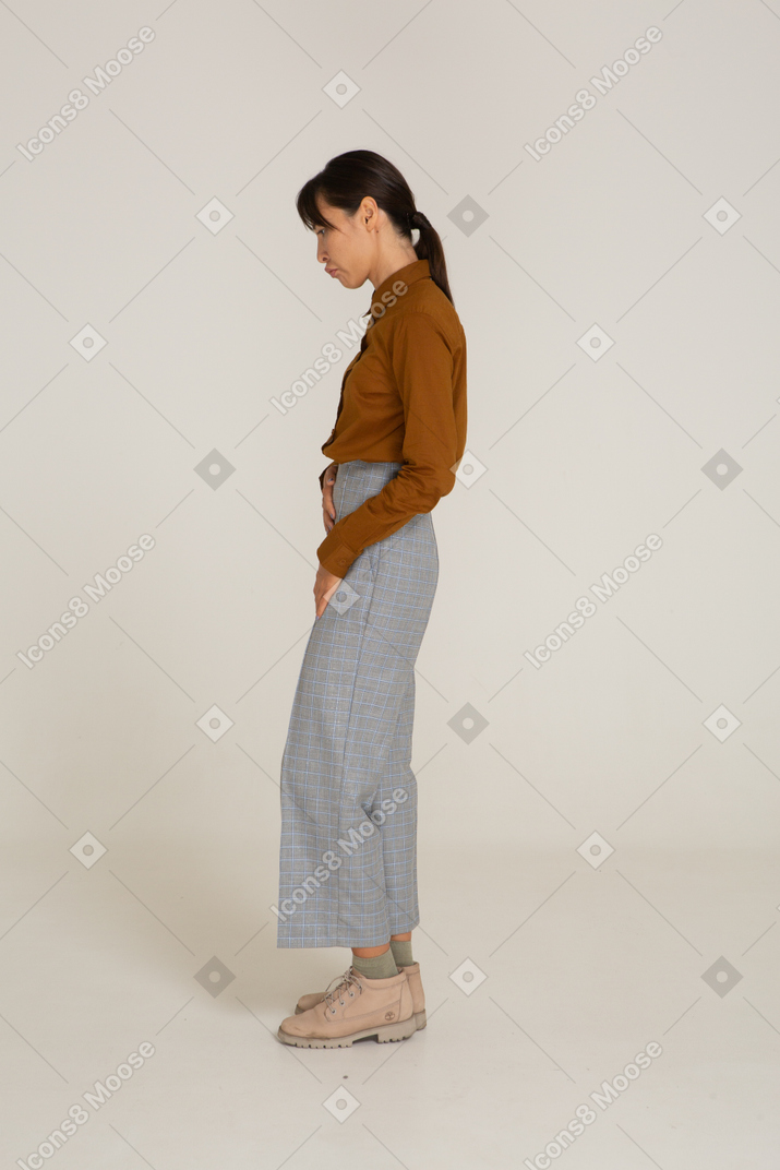 Vista laterale di una giovane donna asiatica in calzoni e camicetta che tocca lo stomaco