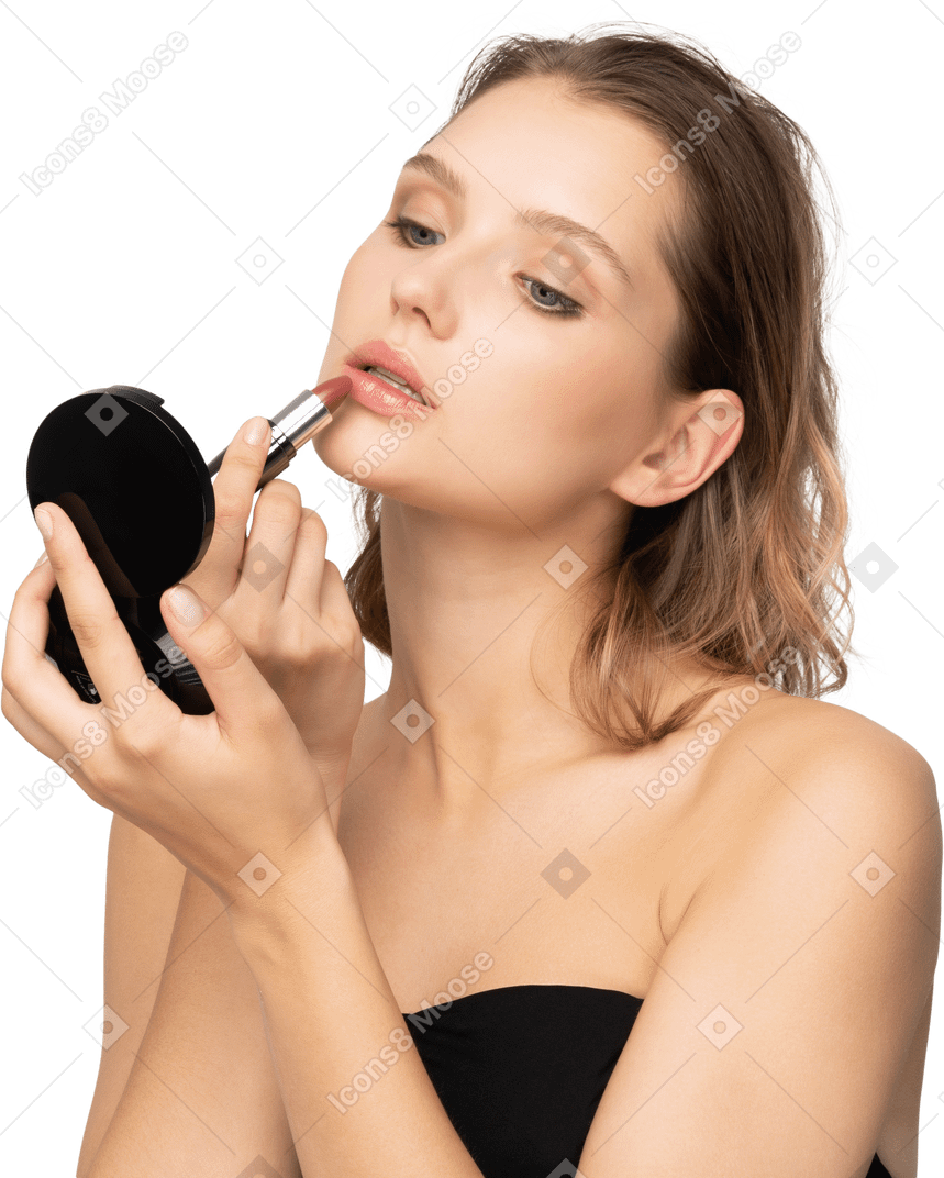Vista frontal de una mujer joven aplicando lápiz labial mientras sostiene un espejo