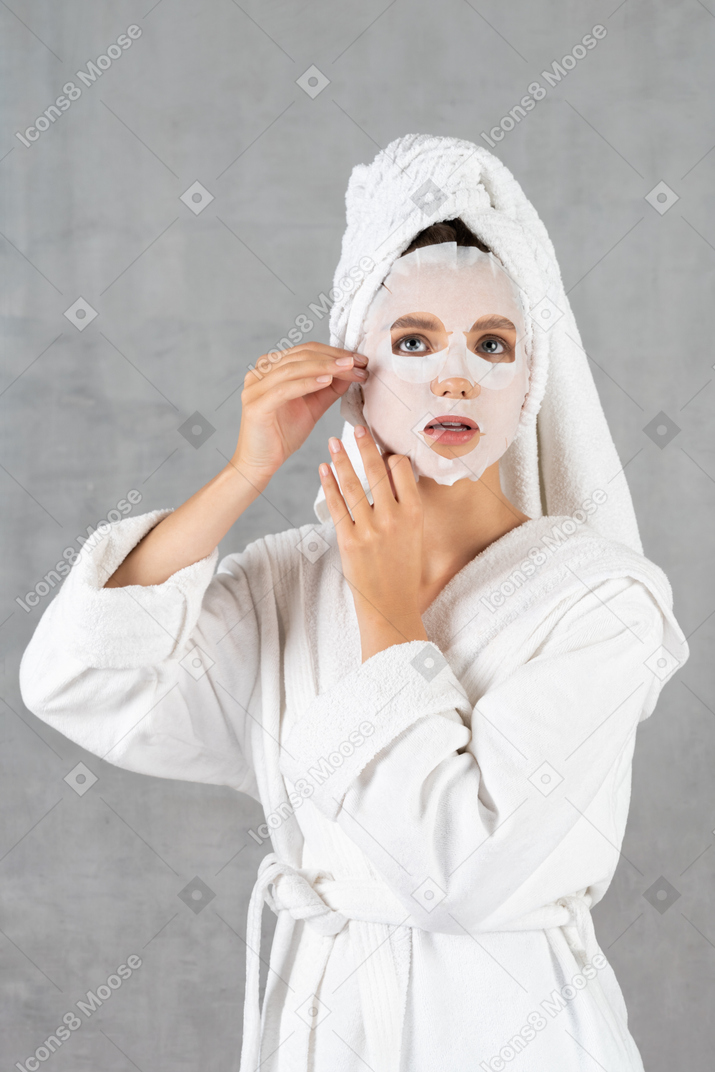 Woman in bathrobe applying face mask
