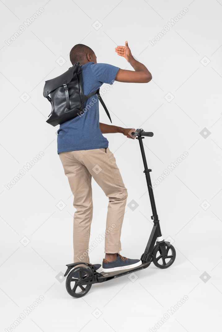 Black male city tourist standing back to camera on scooter and waving