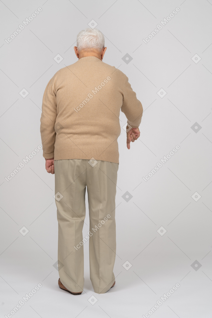 Vista trasera de un anciano con ropa informal apuntando hacia abajo con un dedo