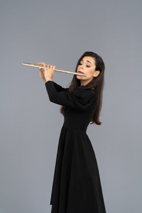 Three-quarter view of a serious young lady in black dress playing the flute