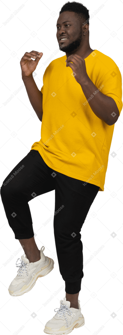 다리를 올리는 노란색 티셔츠를 입은 검은 피부의 젊은 남자의 4분의 3 보기