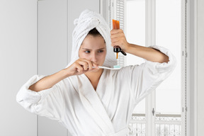 A woman in a robe putting a toothpaste on a toothbrush