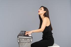Side view of a young lady in black suit sitting and playing the piano