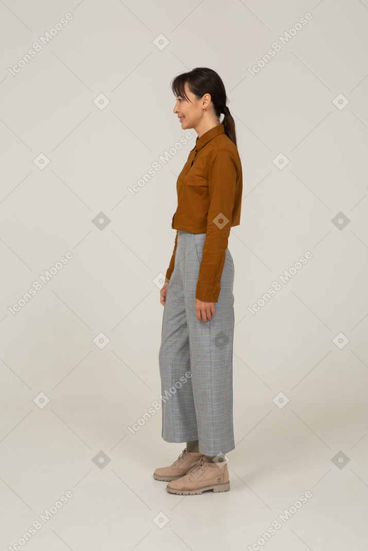 Side view of a smiling young asian female in breeches and blouse standing still