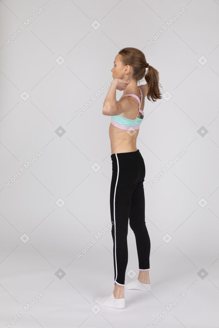 Vista traseira de três quartos de uma adolescente em roupas esportivas levantando as mãos