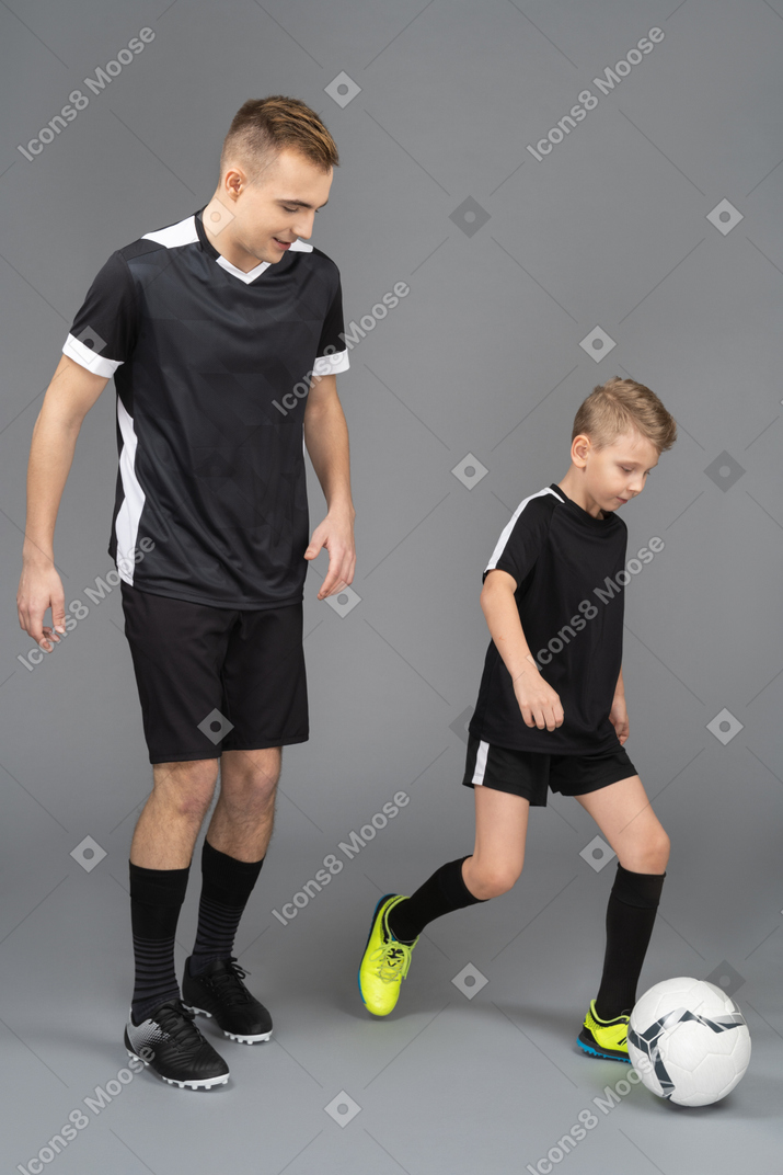 Full-length of a young man coaching little boy how to play fooyball