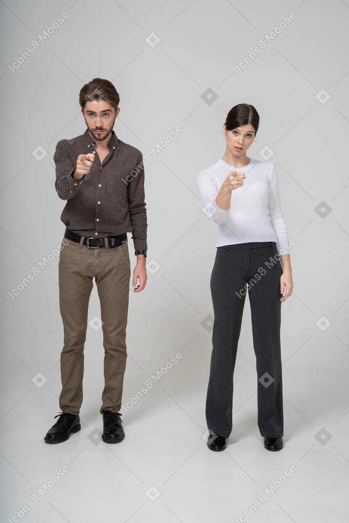 一对穿着办公室服装的年轻夫妇的前视图，手指向前