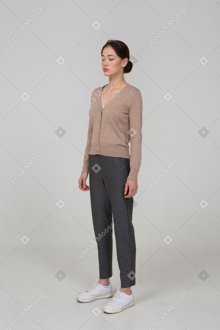 Three-quarter view of a young lady standing still in pullover and pants with her eyes closed