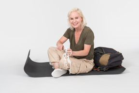 Mature female tourist sitting on tourist mat near the backpack