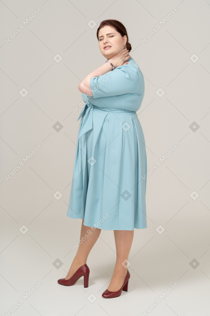 Vista laterale di una donna in abito blu che soffre di dolore al collo