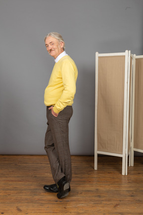 Side view of a smiling old man putting hand in pocket while looking at camera