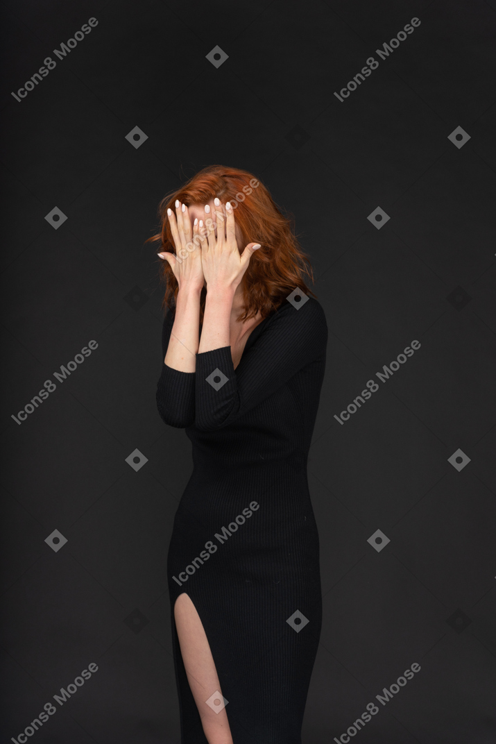 A frontal view of the sexy young girl dressed in black and covering her face with hands