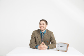 Handsome young man sitting near the clock with his hands folded